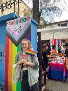 Julia Behrens auf der Hanoi Pride 2022 Julia Behrens steht vor einer Pride-Fahne mit der Aufschrift "Hanoi Pride 2022"